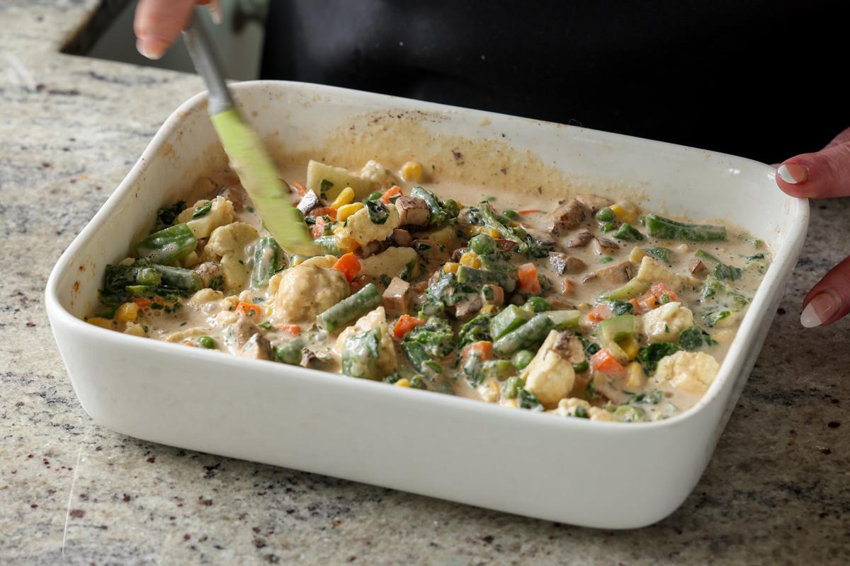 mixing the veggies with the sauce in the casserole dish