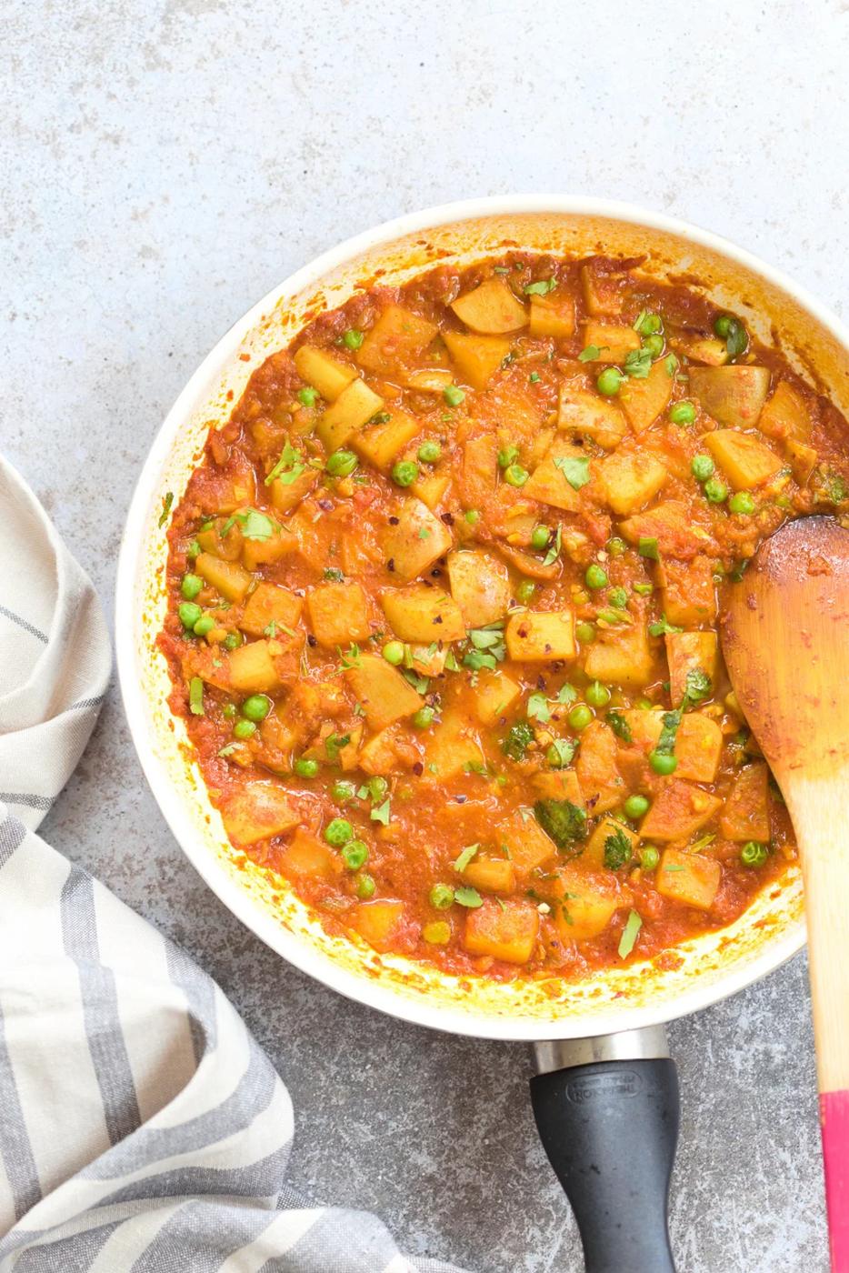 overhead shot of a white skillet with vegan aloo matar with peas and potatoes