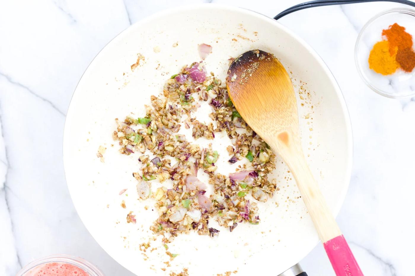 garlic, onion and chili being added to toasted spiced in a white skillet