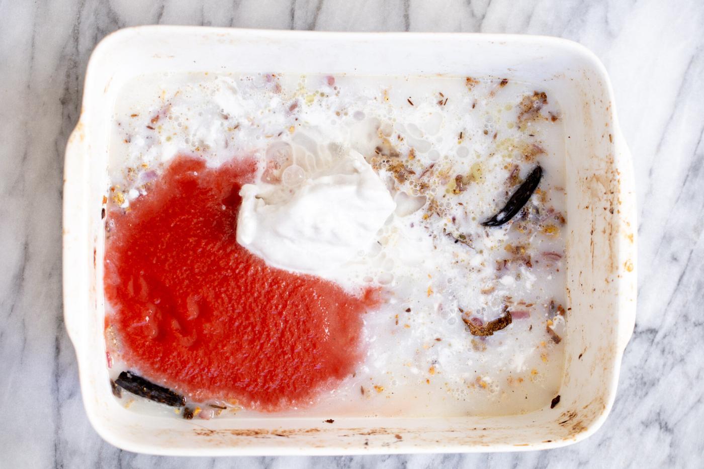 coconut milk and tomato puree being added to a casserole dish