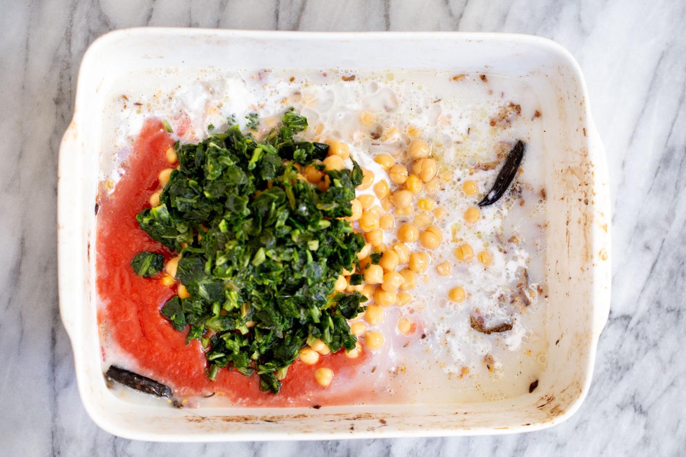 spinach and chickpeas being added to a casserole dish