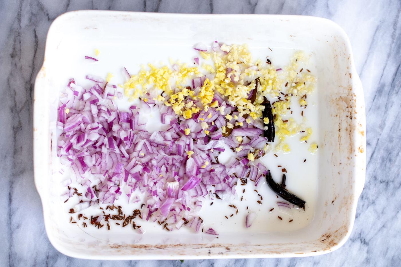 onions and ginger being added to casserole dish with toasted spices