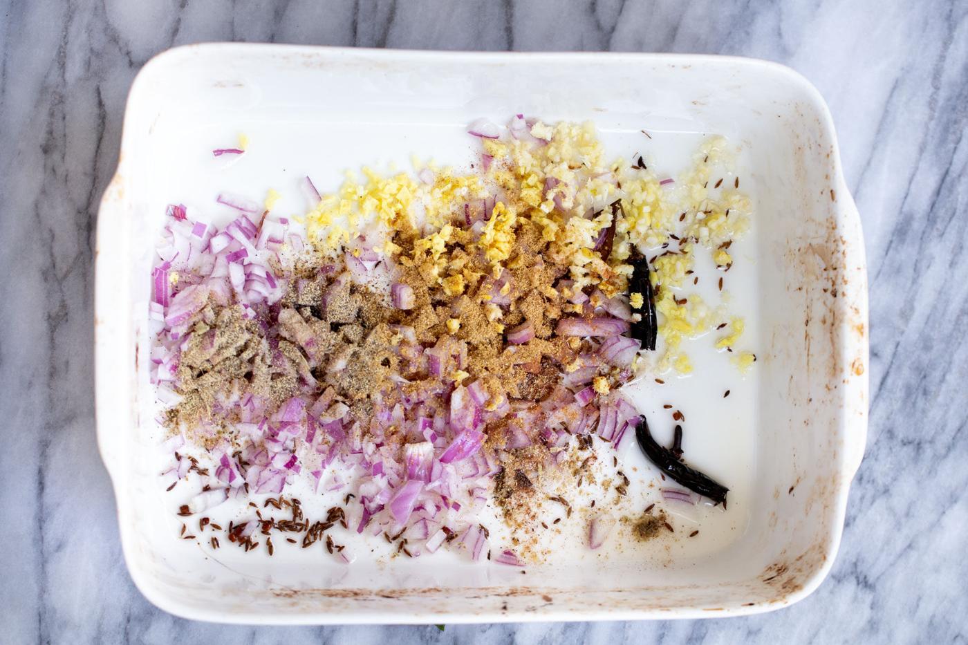dried spices being added to onion and ginger in a casserole dish