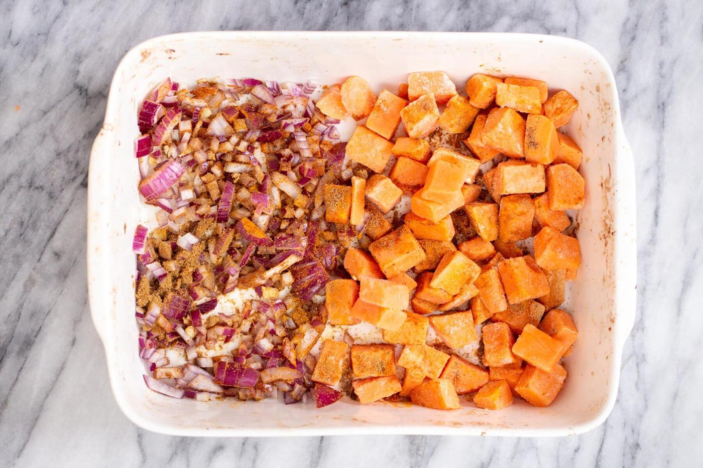 a casserole dish with sweet potato cubes on one side, and onions, garlic and ginger on the other side