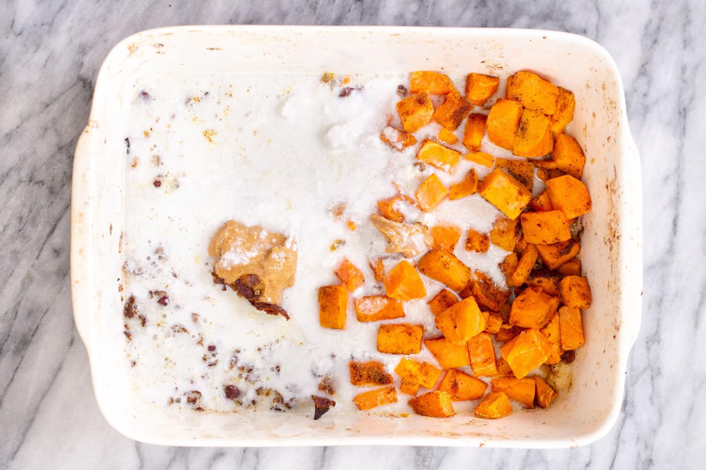 coconut milk and peanut butter being added to a casserole dish with roasted sweet potato