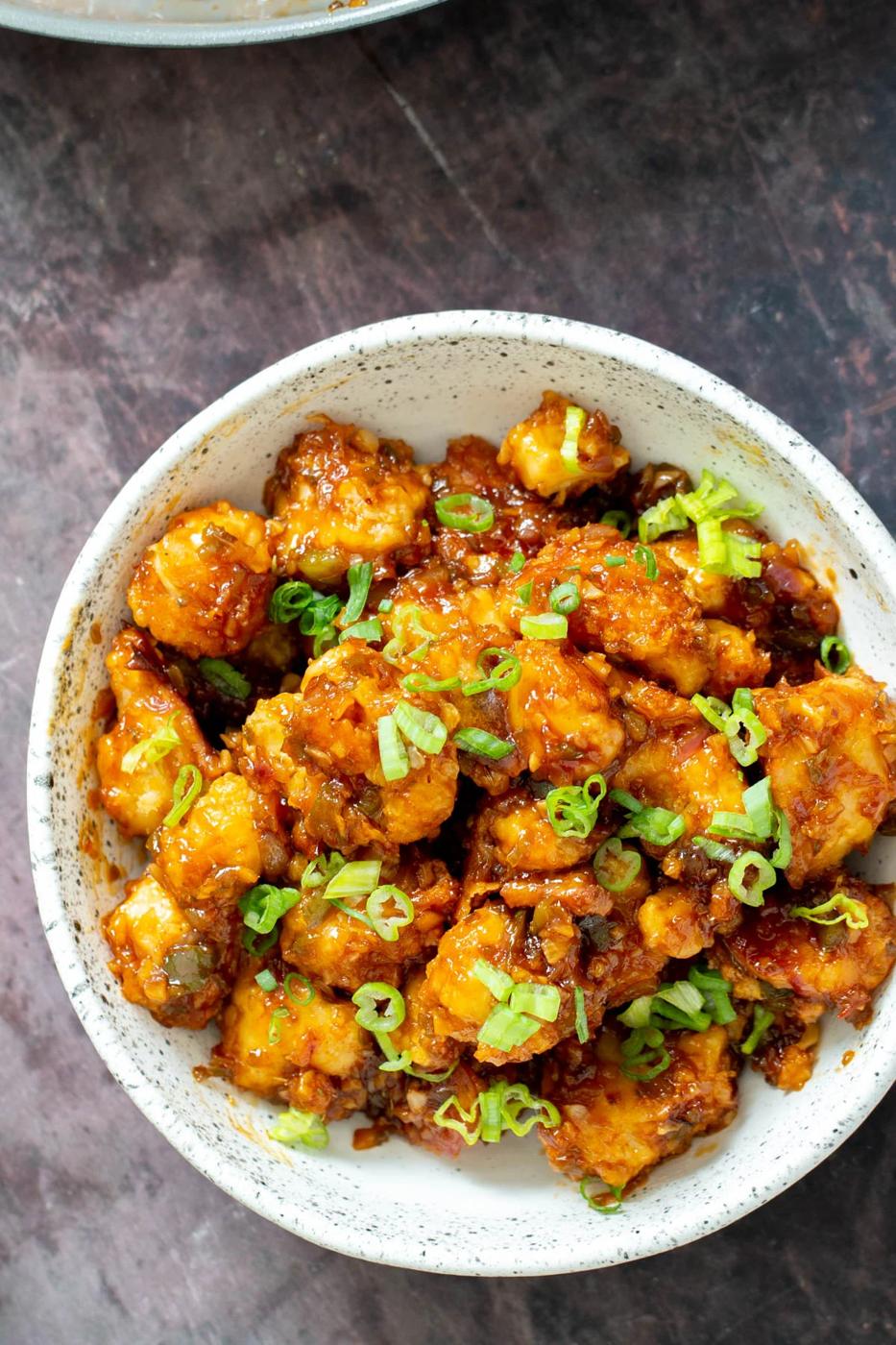 a white bowl with vegan gobi Manchurian topped with thinly sliced scallions
