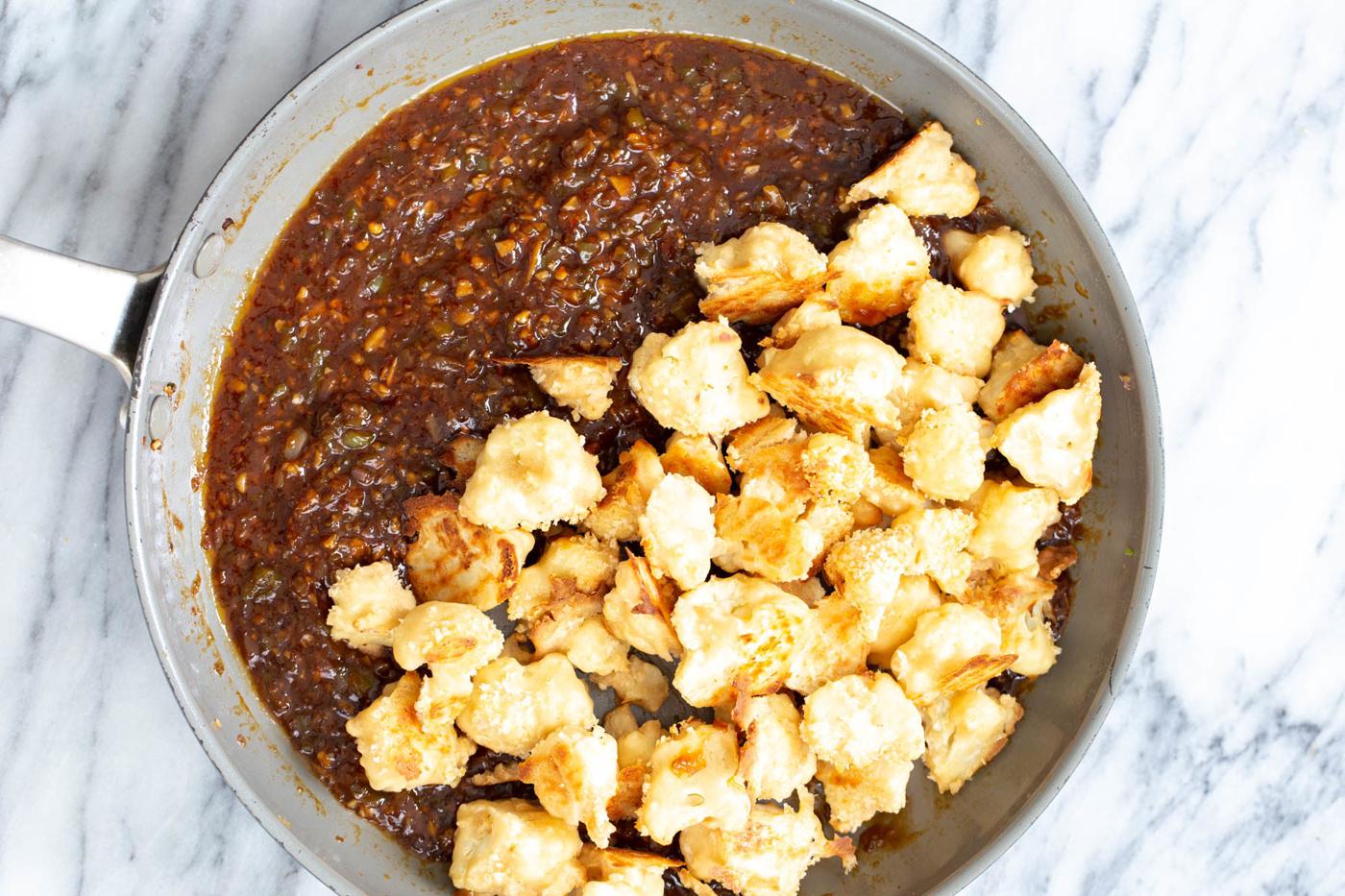 breaded baked cauliflower florets being added to Manchurian sauce in a pan
