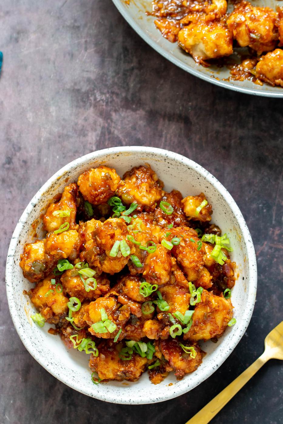 a serving of cauliflower manchurian in a white bowl with a golden fork on the side