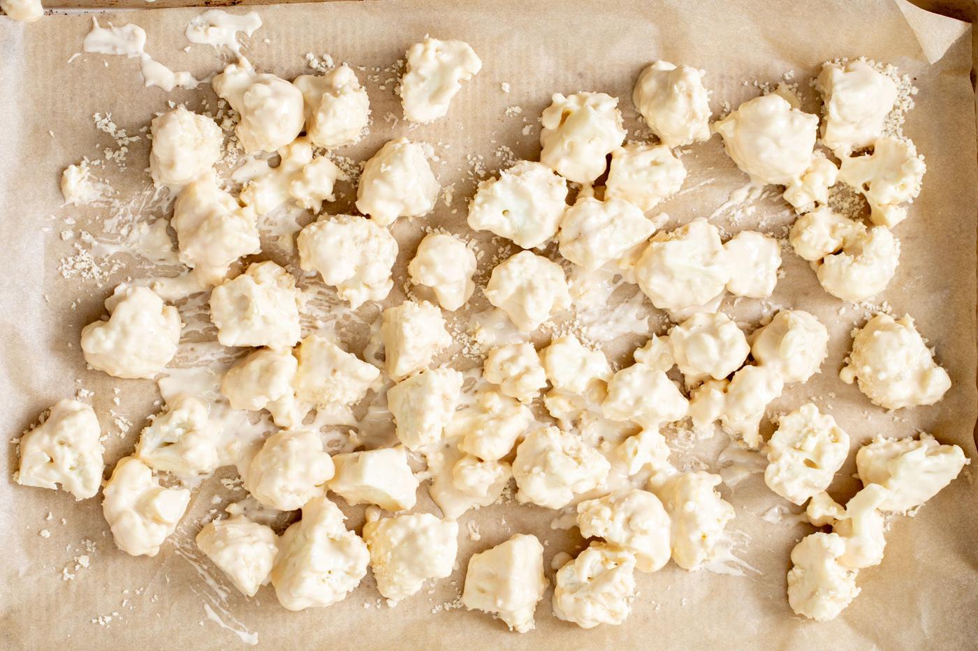 battered cauliflower florets on a lined baking sheet