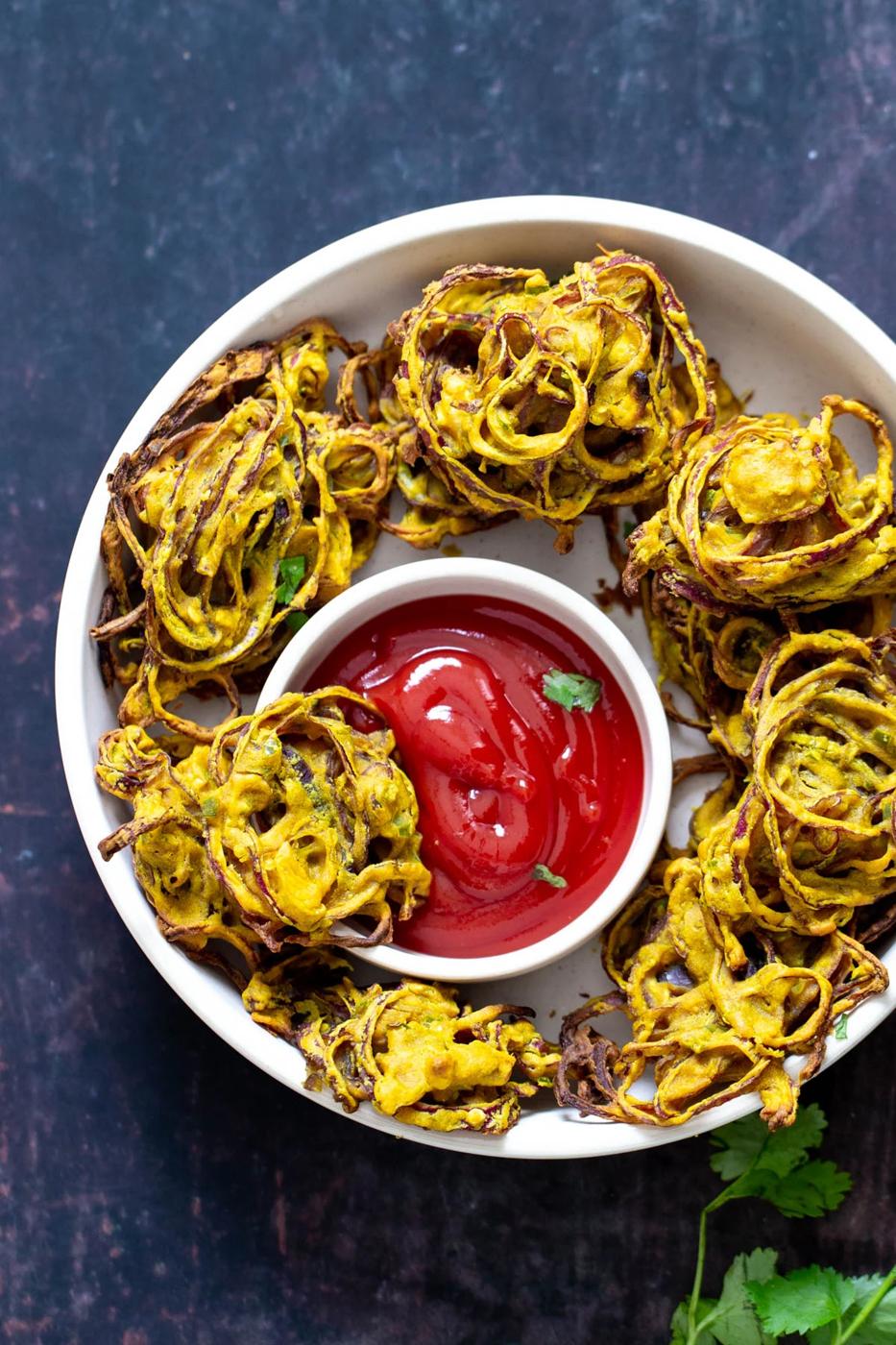 a platter with onion pakora served with a small side dish of ketchup