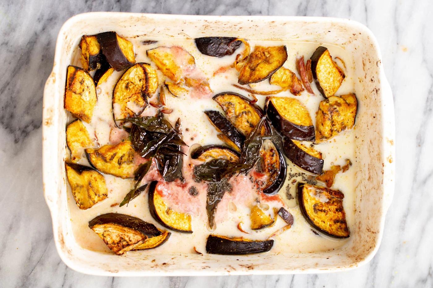 coconut milk being added to white casserole dish with baked aubergines