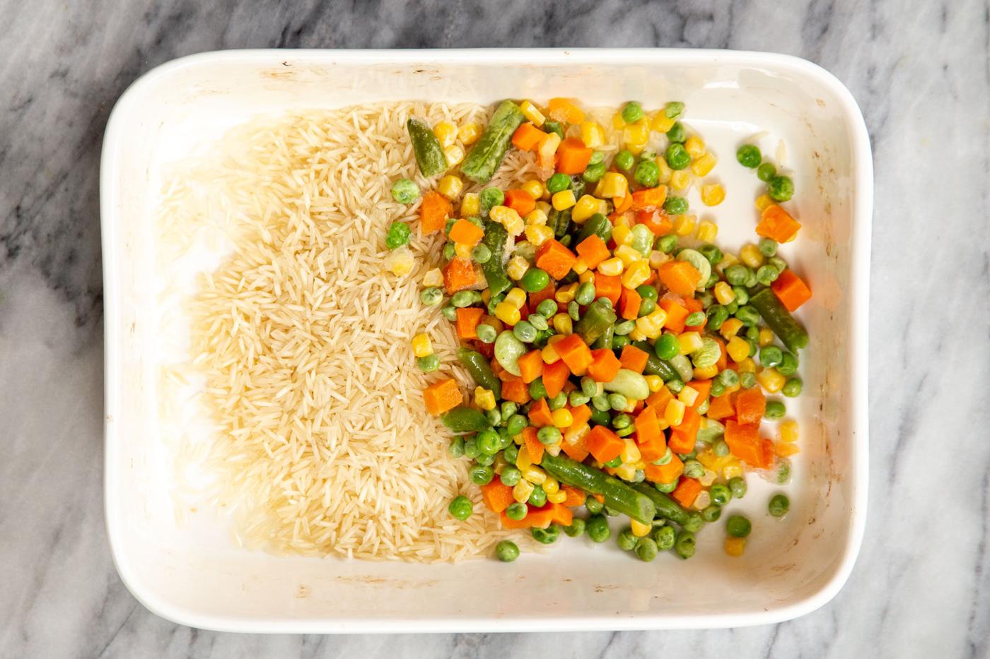uncooked rice and frozen veggies in a white casserole dish