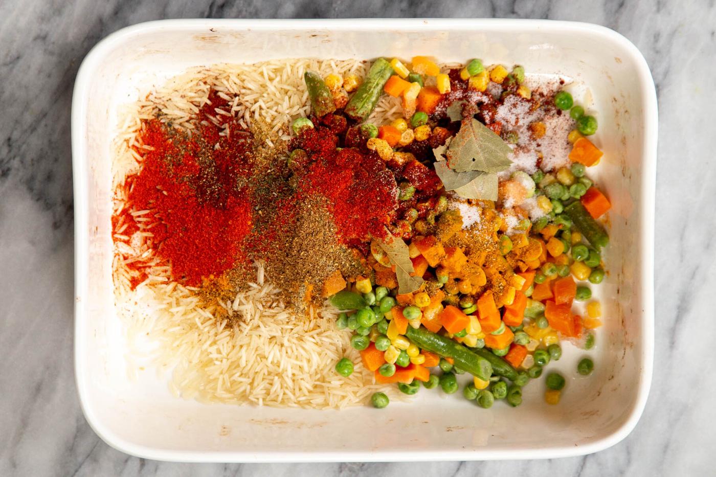 a white casserole dish with spices, rice and veggies
