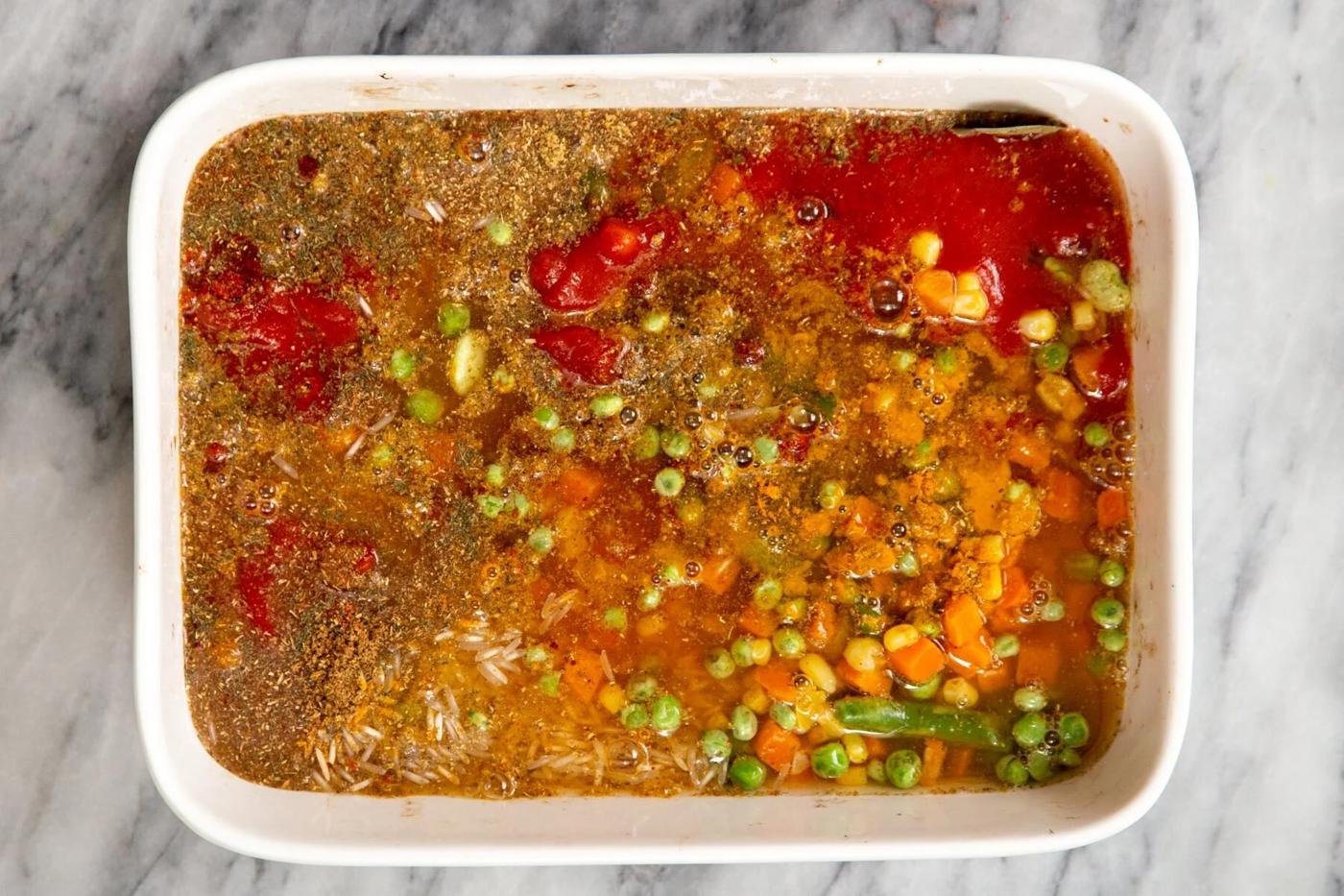 dry and liquid ingredients for baked masala rice pulao in a white casserole dish