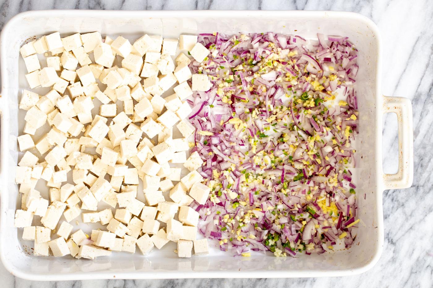 tofu cubes in a casserole dish next to minced onion, ginger, garlic and chile