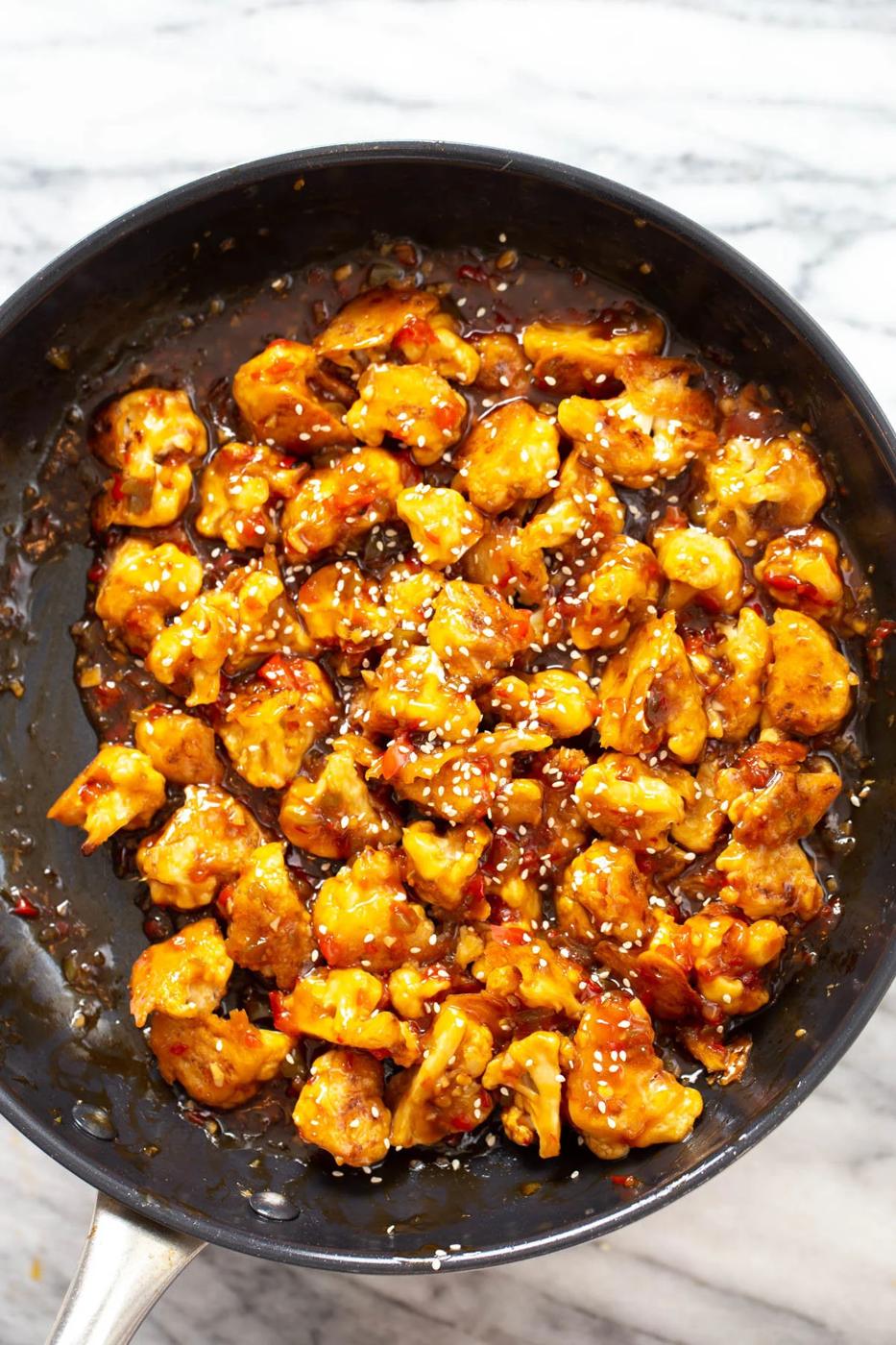 general tso cauliflower being tossed in sweet and sticky sauce
