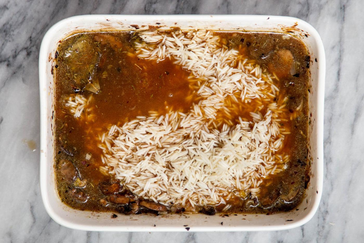 rice, mushrooms and broth in a white casserole dish