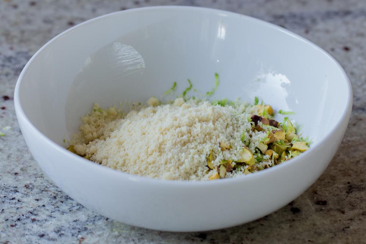 adding almond flour to the bowl of chopped pistachios