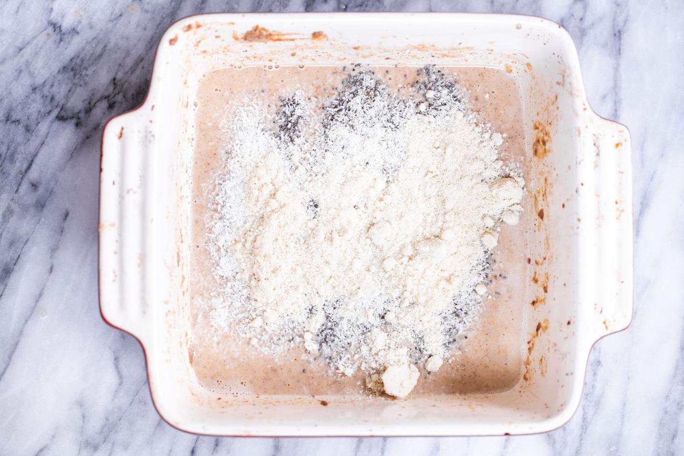 almond flour and chia seeds being added to casserole dish with banana batter