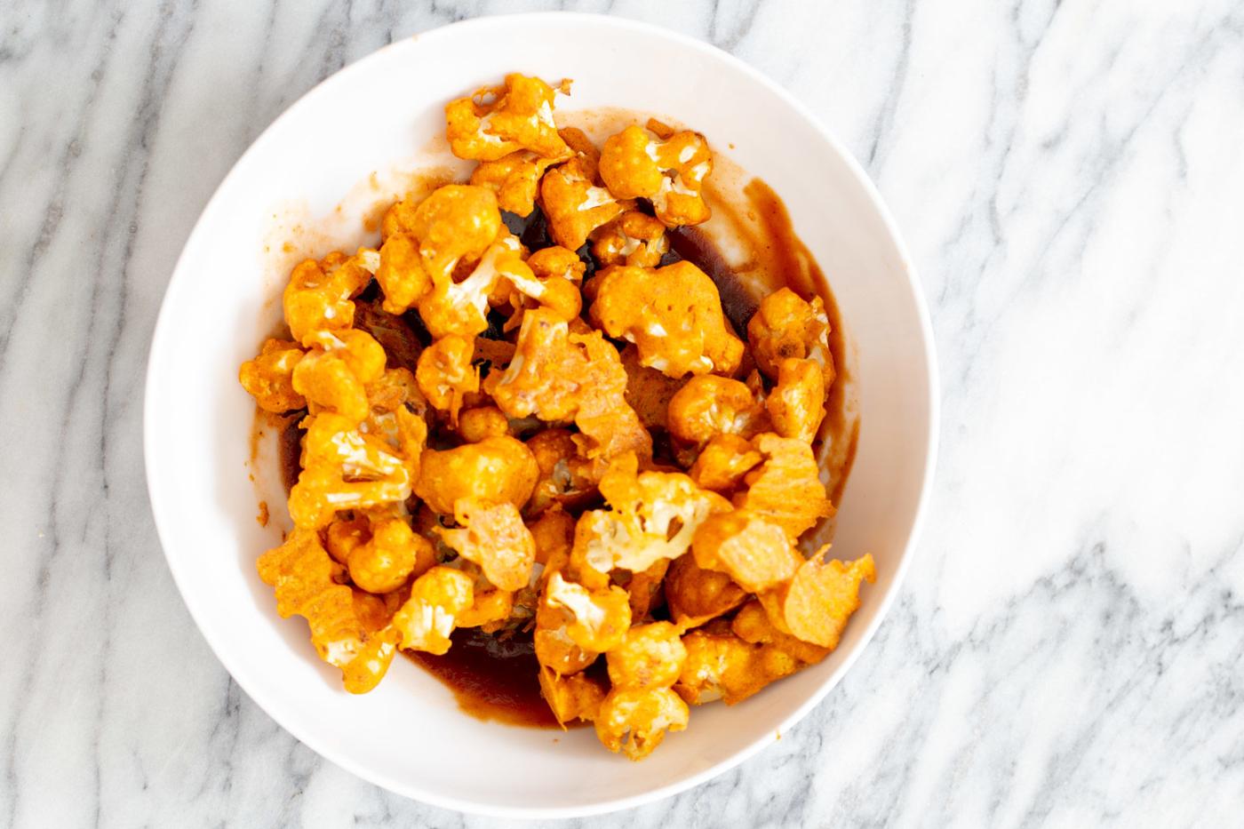 beer battered baked cauliflower wings being tossed in hot sauce and bbq sauce