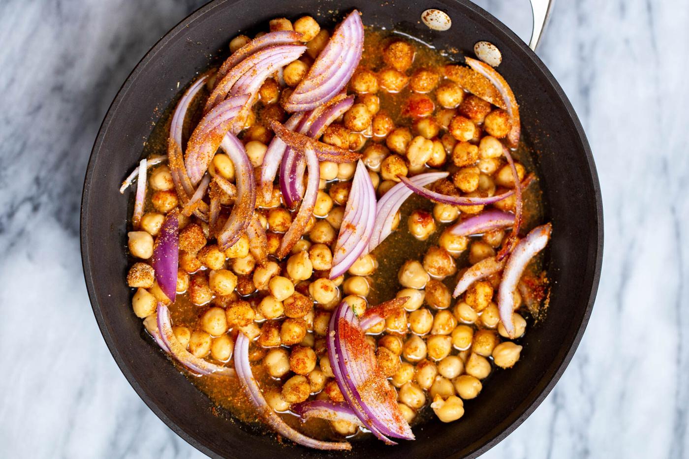 chickpeas with onions and spice blend in a black sauteeing pan