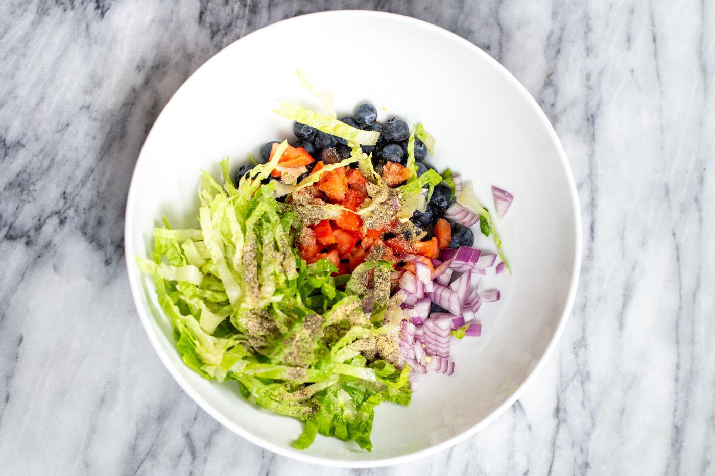 lettuce, blueberries, tomatoes and onion in a white bowl