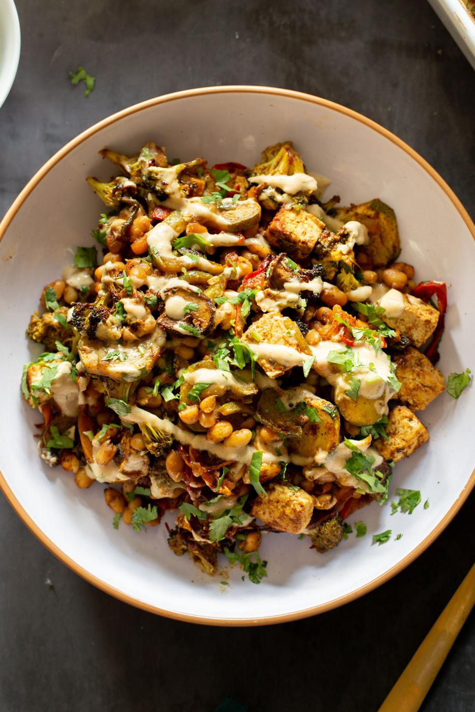 a bowl of baked veggies and tofu seasoned with berbere and drizzled with creamy tahini sauce