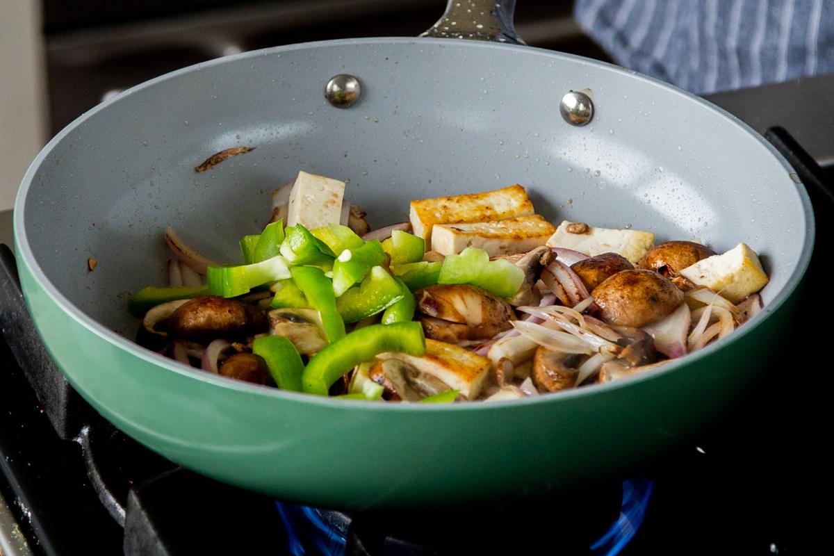 adding bell peppers to the pan of tofu