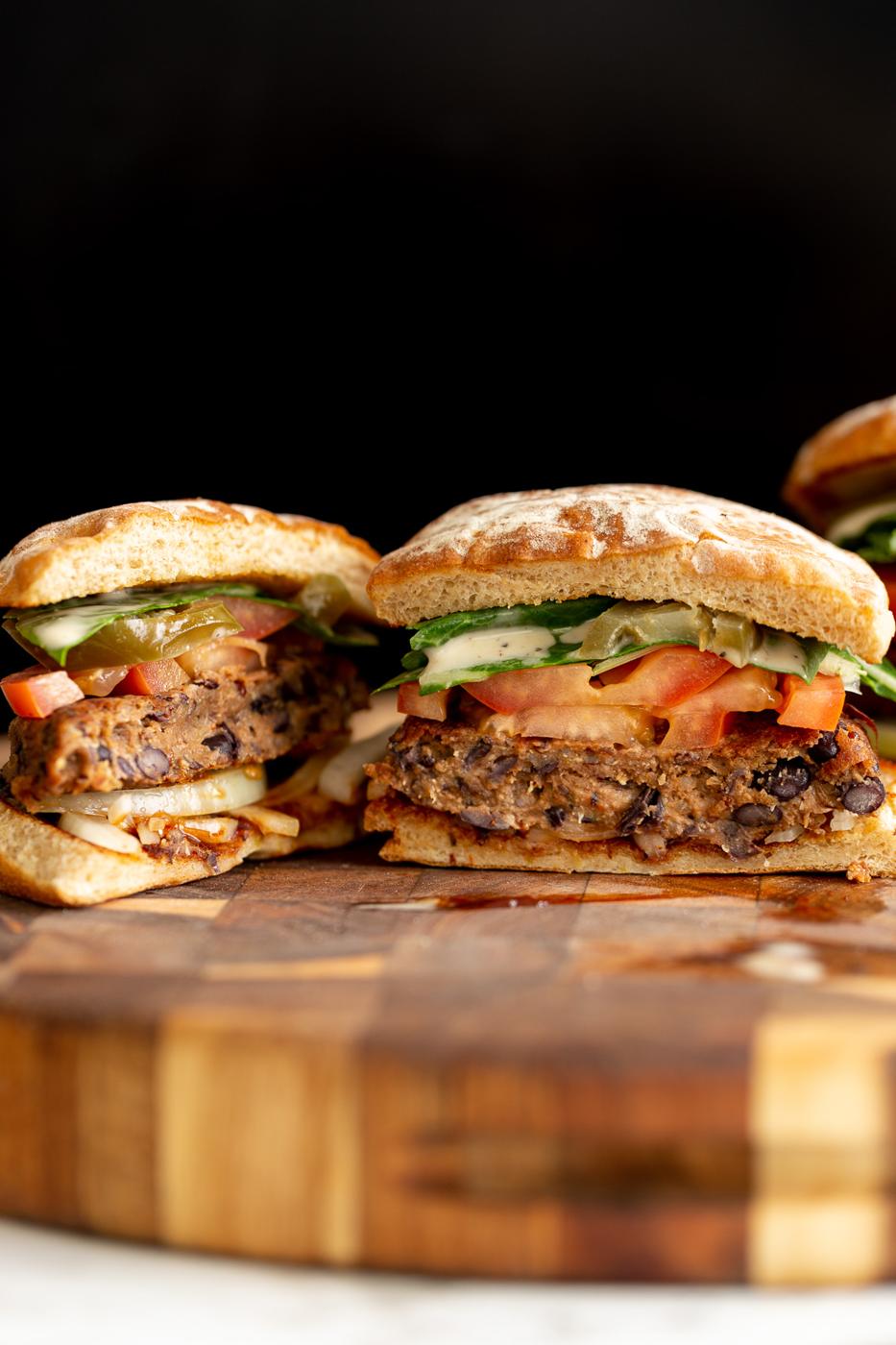 a halved vegan black bean quinoa burger topped with tomato slices and drizzled with ranch sauce