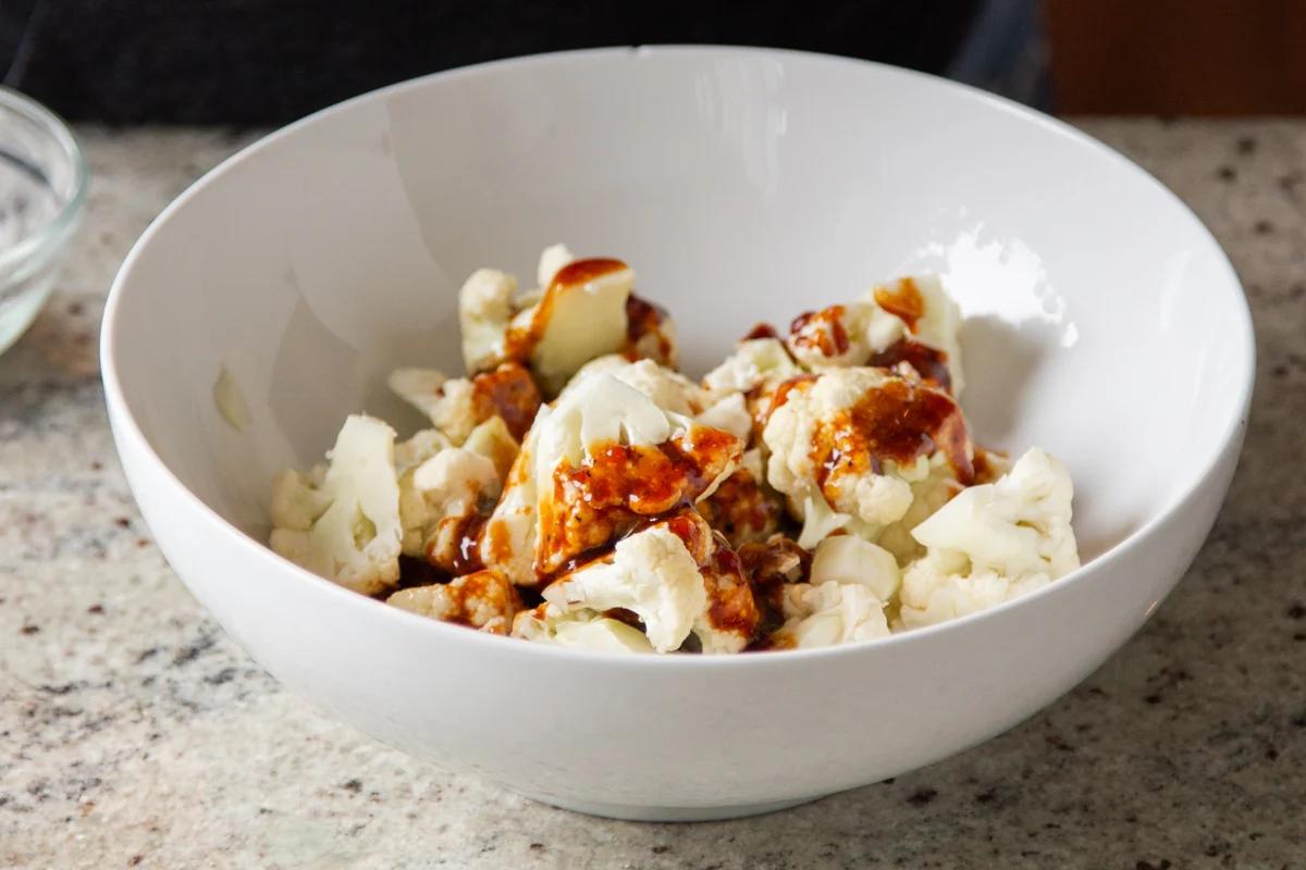 cauliflower florets in a small bowl being drizzled with spicy sauce
