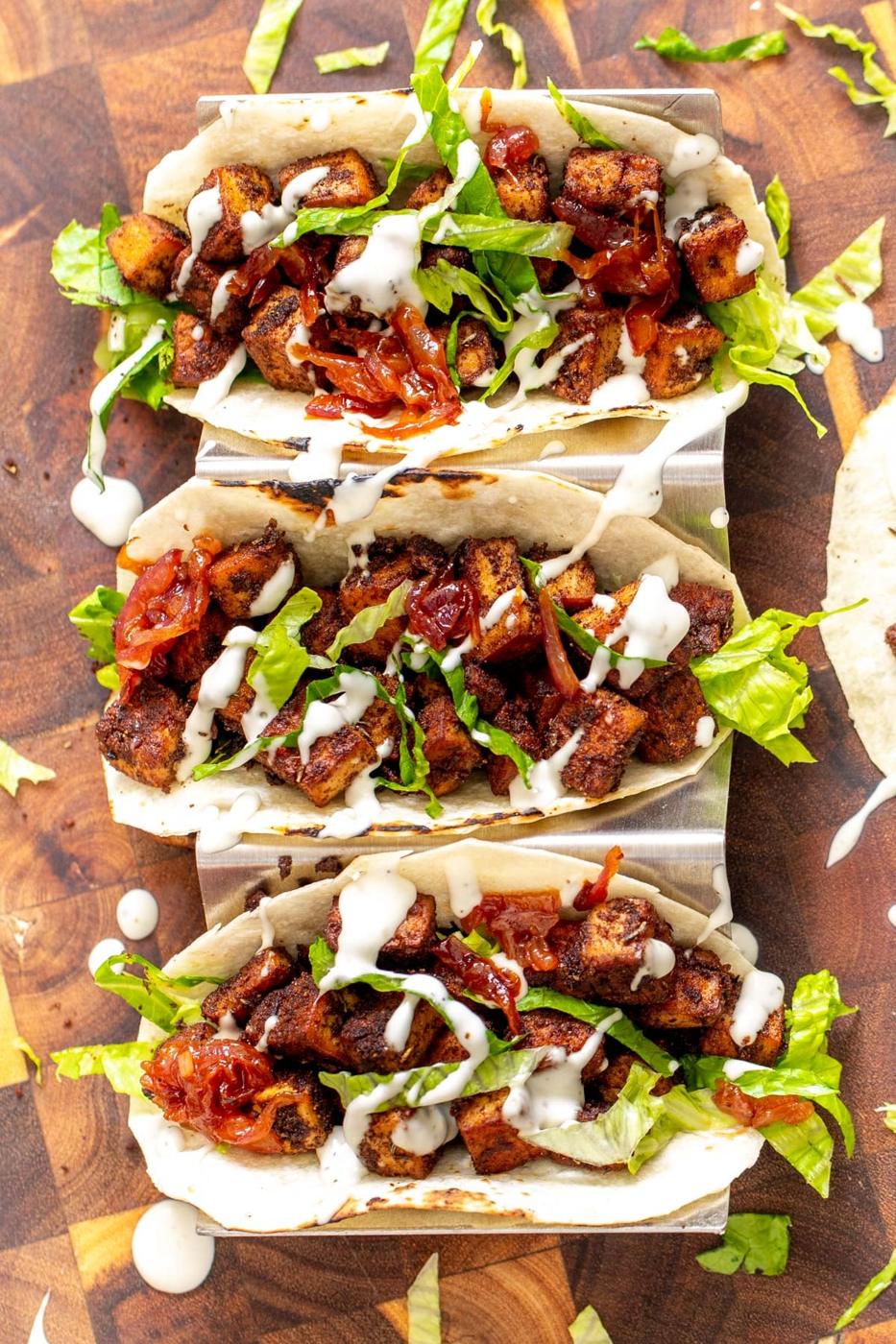 overhead shot of blackened tofu tacos drizzled with sour cream and topped with caramelized onions