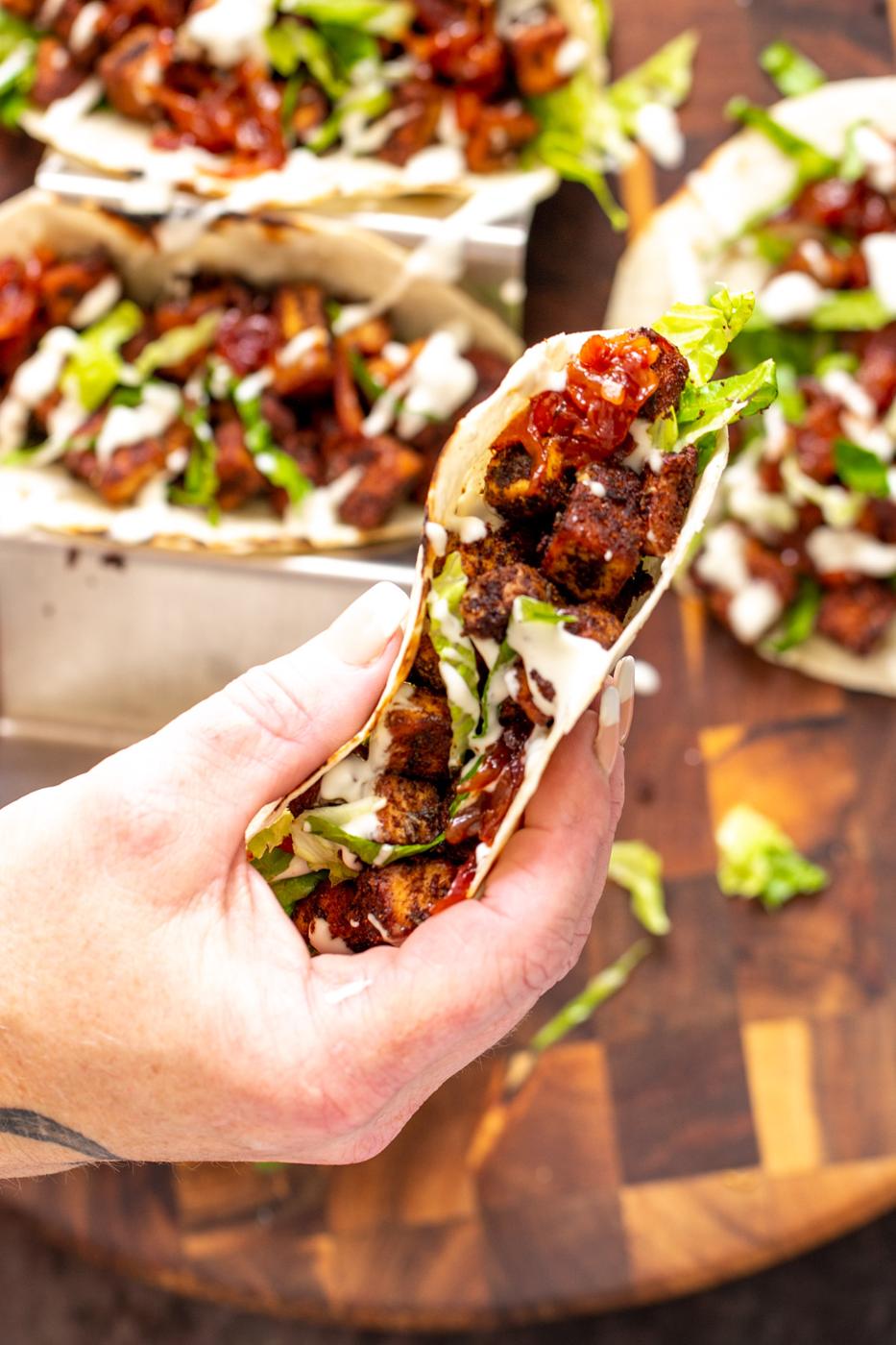 a hand holding a vegan blackened tofu taco drizzled with sour cream and filled with caramelized onions