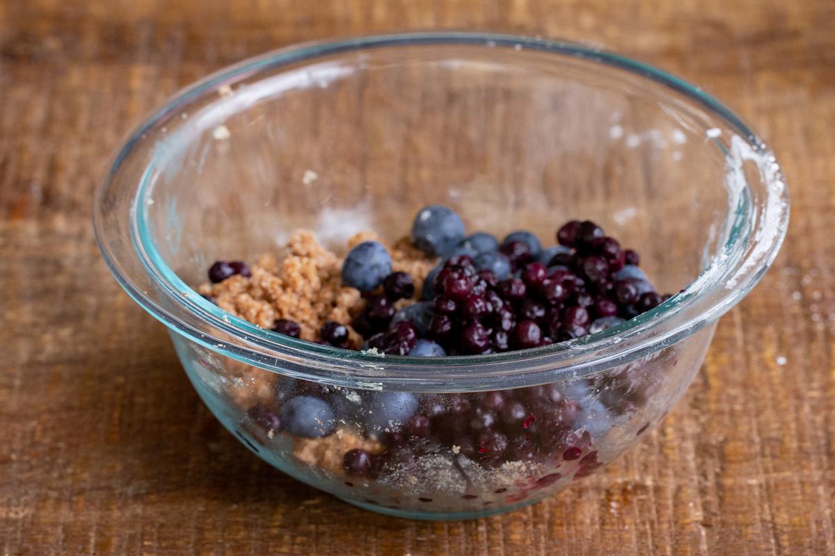 fresh and frozen blueberries being added to streusel dough