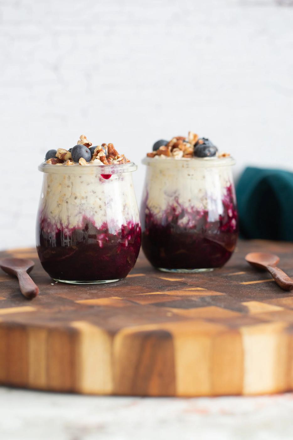 side view of two jars of make ahead vegan blueberry muffin overnight oats on wooden board