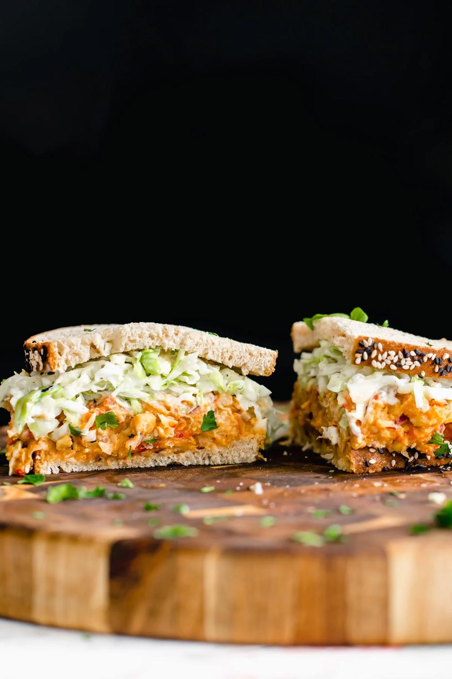 a halved buffalo chickpea salad sandwich with slaw on a wooden chopping board