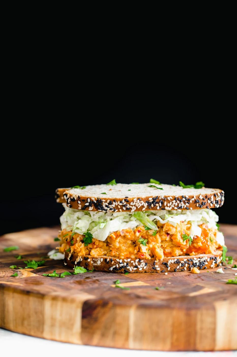 side view of vegan buffalo chickpea salad sandwich on a wooden board