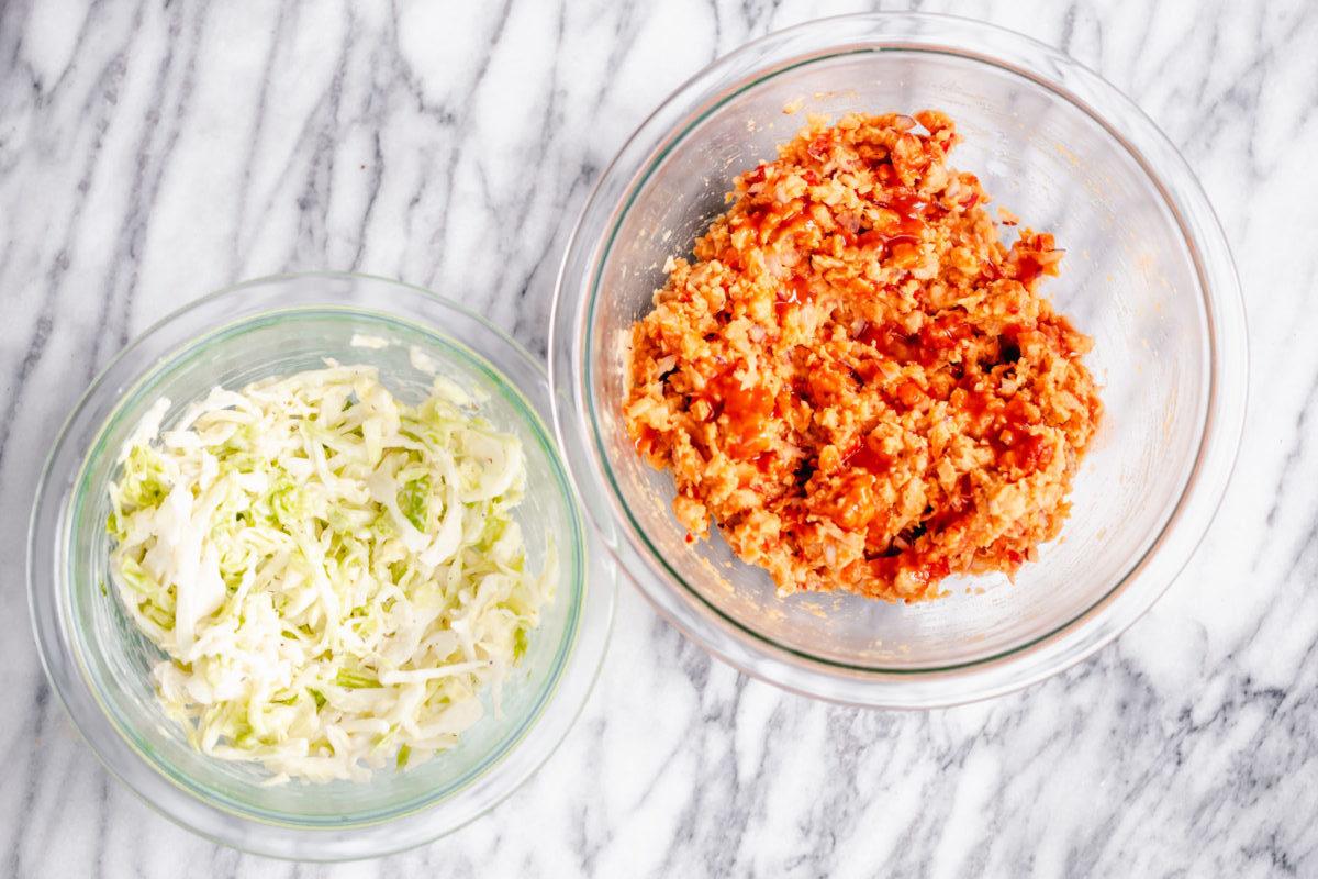 slaw and buffalo chickpea salad in two glass bowls on a marble countertop