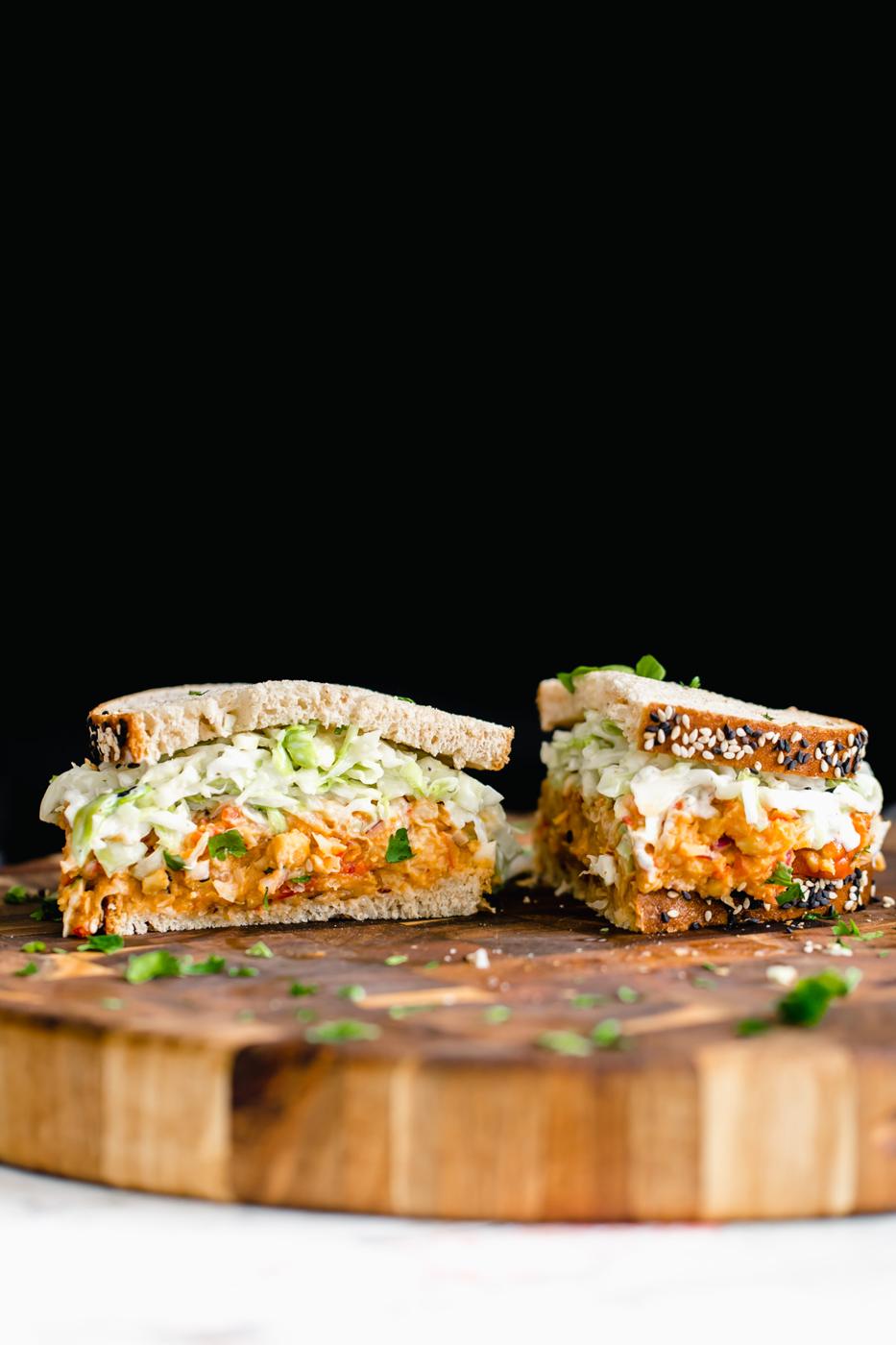a halved chickpea salad sandwich on a wooden board