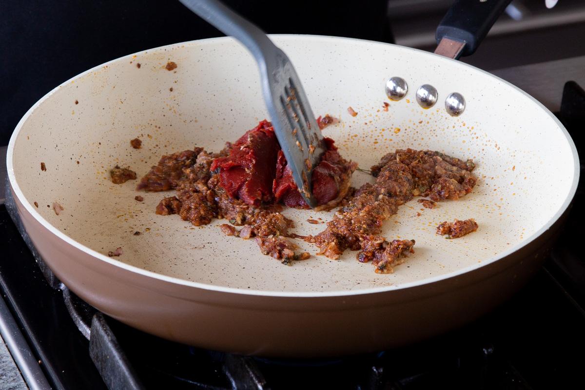 adding tomato paste to the frying pan