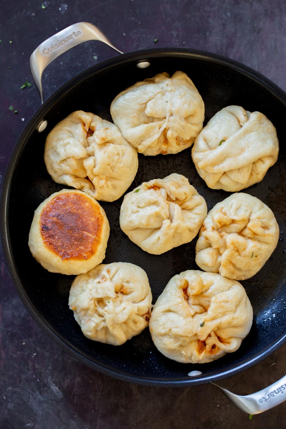 cooked bao in a pan, with one flipped over so you can see the crispy bottom