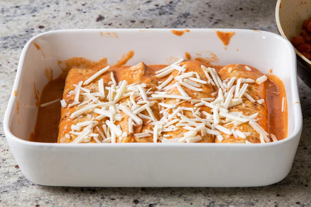 butter chicken enchiladas in the baking pan topped with vegan cheese, before baking