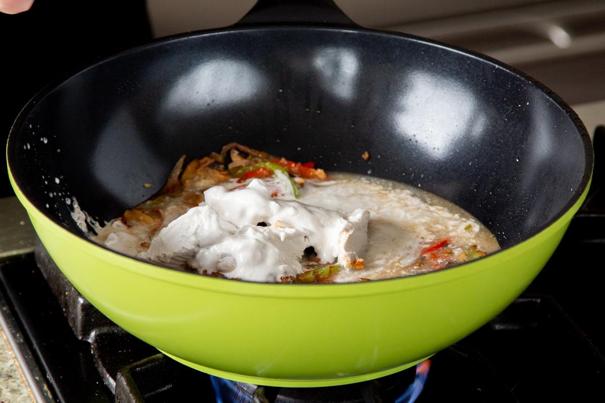 adding coconut milk to the wok with the veggies and spices
