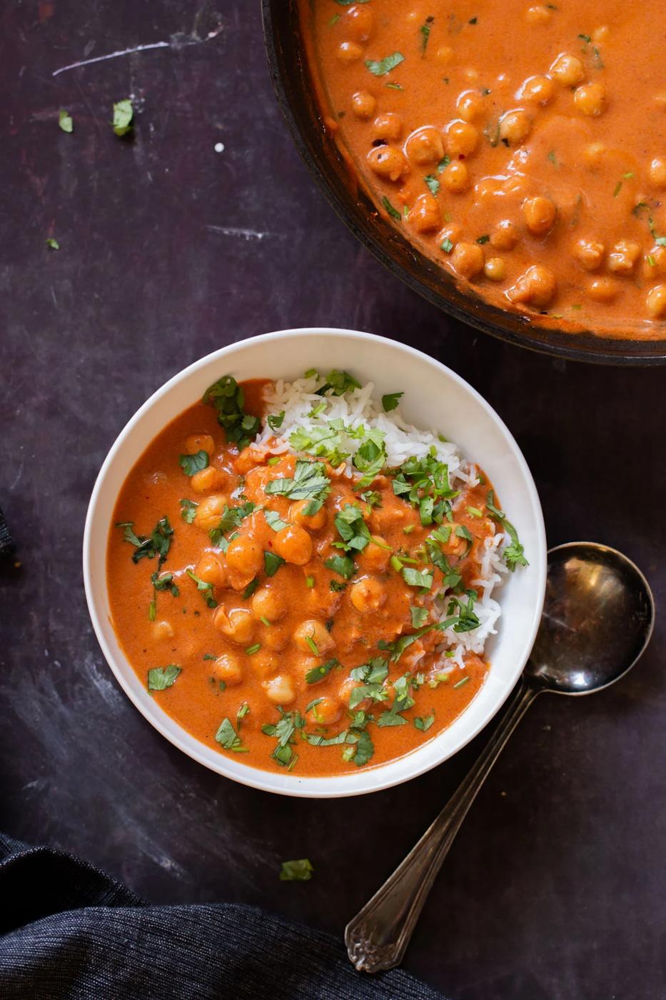 white bowl of butter chickpeas over rice with cilantro on top next to the skillet