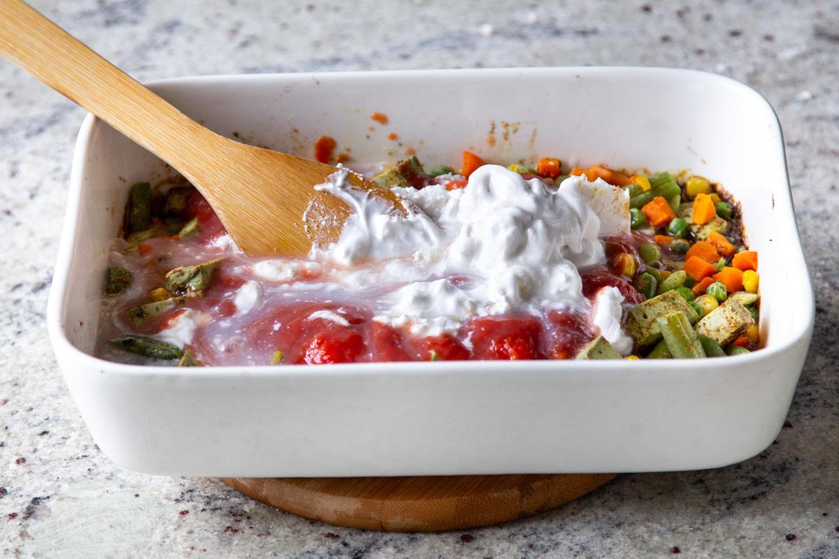 adding tomatoes and coconut milk to the veggies and tofu in the pan