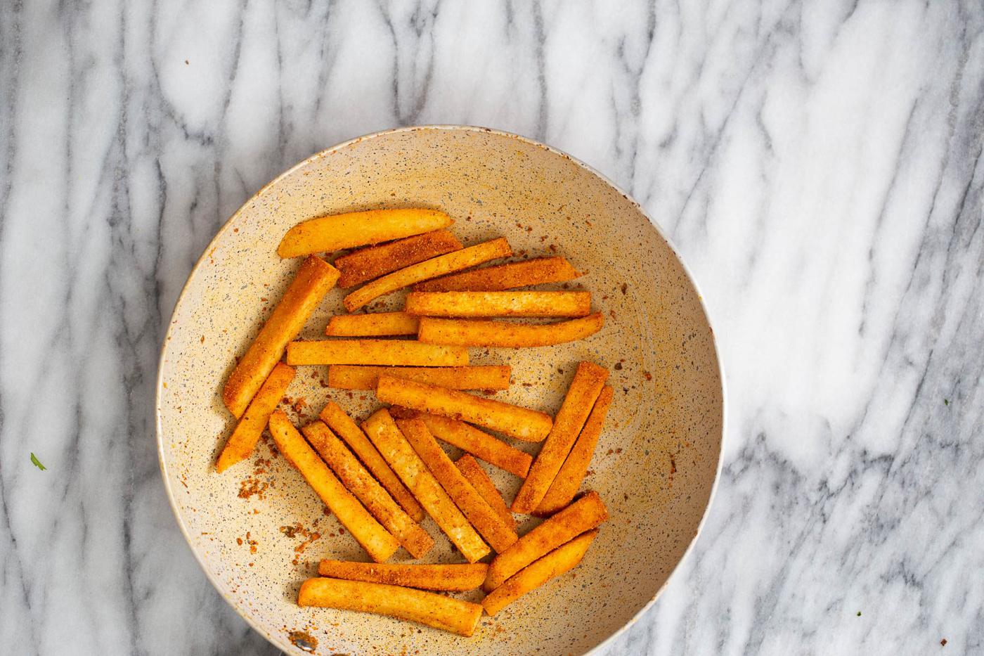 pan fried chickpea flour fries being tossed in salt and Cajun seasoning