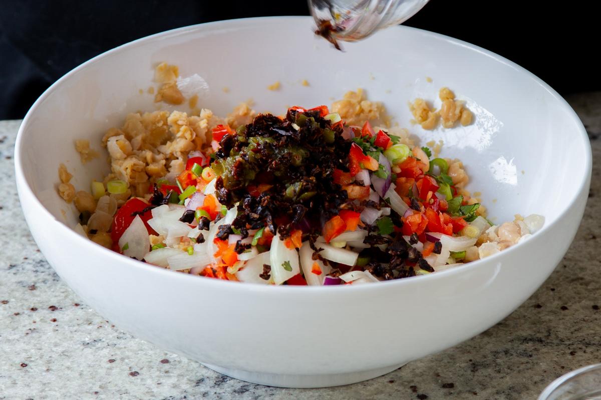 adding sun-dried tomatoes and spices to the bowl of mashed chickpeas and veggies
