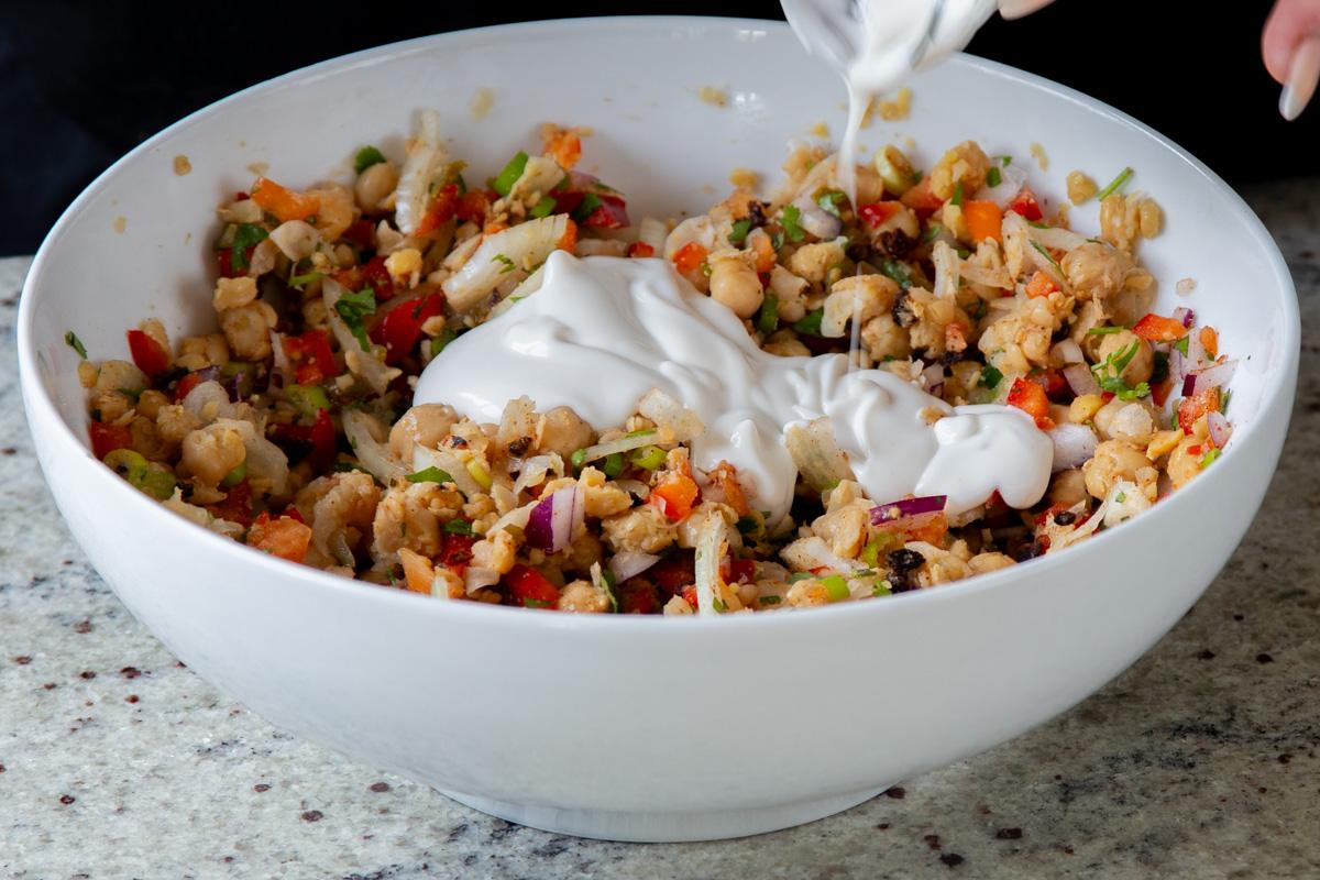 adding vegan yogurt and lime juice to the chickpea-veggie mixture