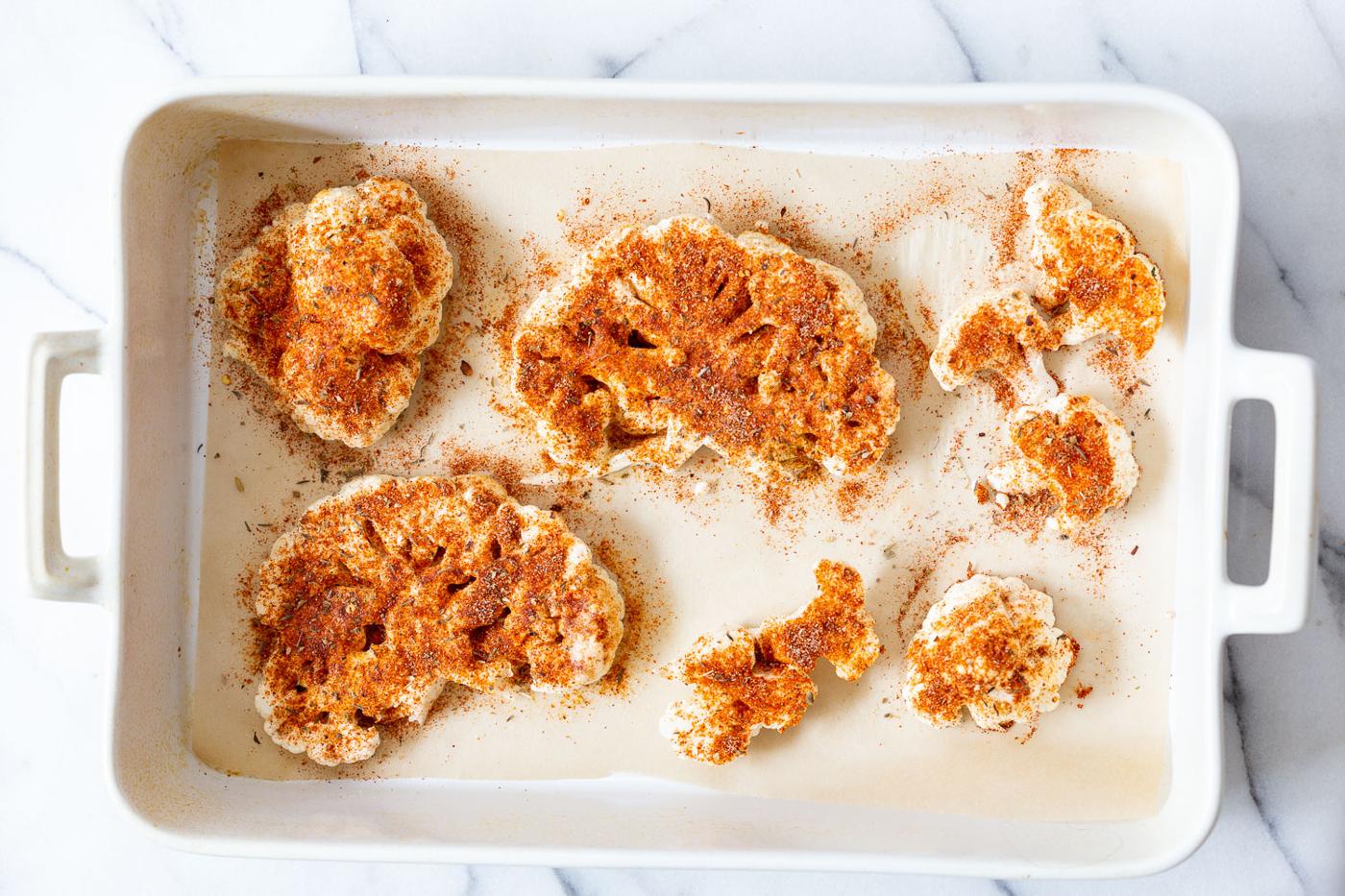 Cauliflower Slices on parchment lined baking dish for our Cajun Roasted Cauliflower Steaks