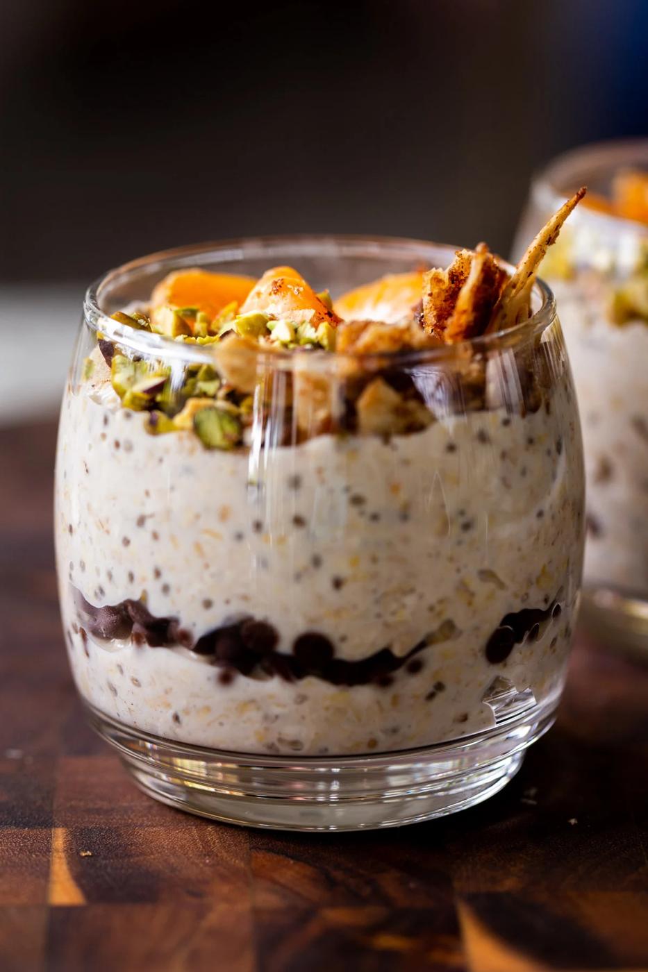 side shot of cannoli overnight oats in a glass topped with oranges, pistachios, and crispy cinnamon sugar tortilla pieces, so you can see the chocolate chips layer