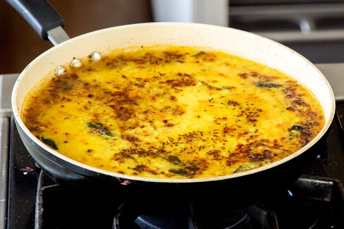 tempered oil being poured over a pan with yellow lentil dal
